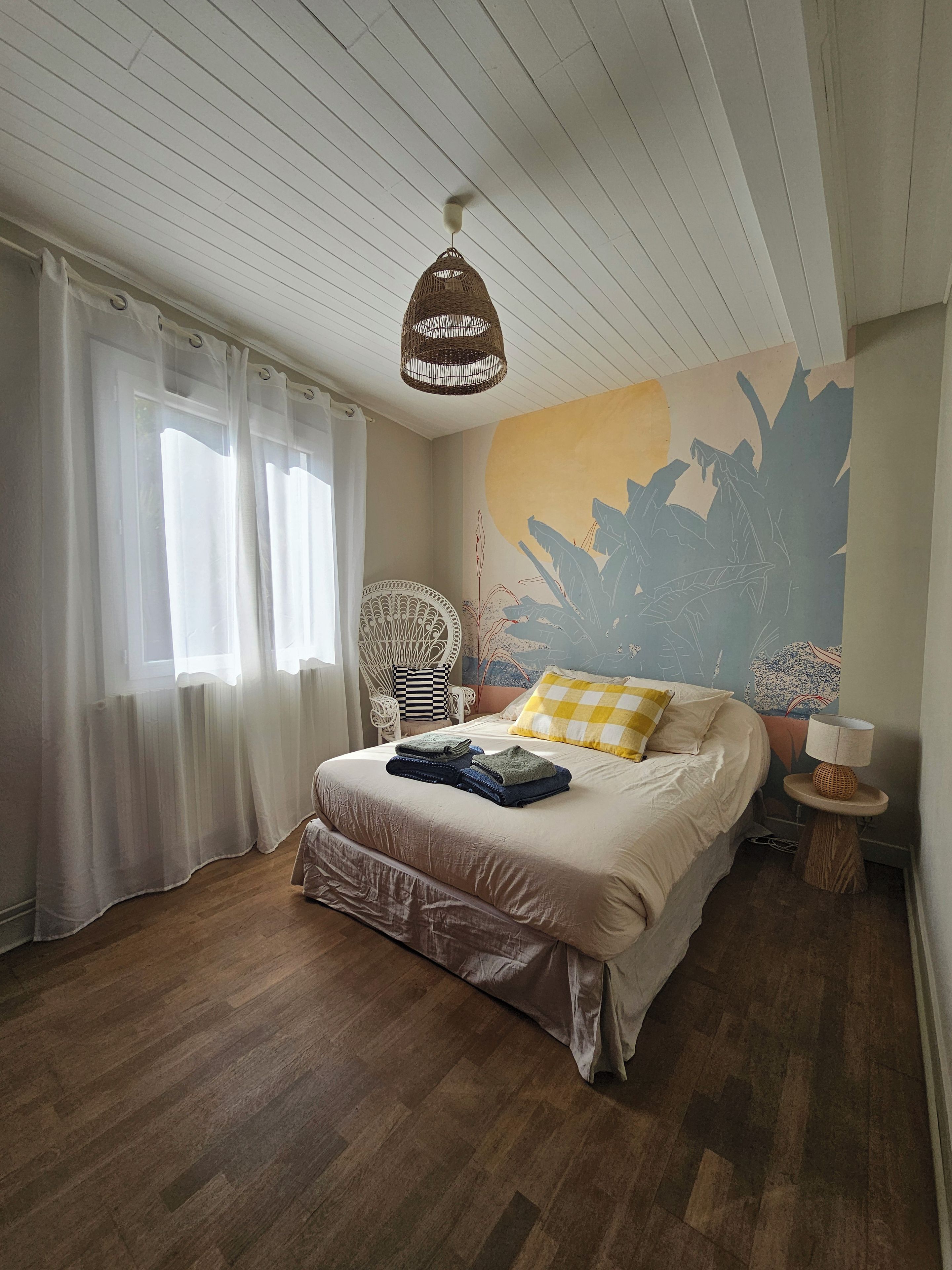 Un dormitorio con cama, una silla, una lámpara y un mural en la pared.