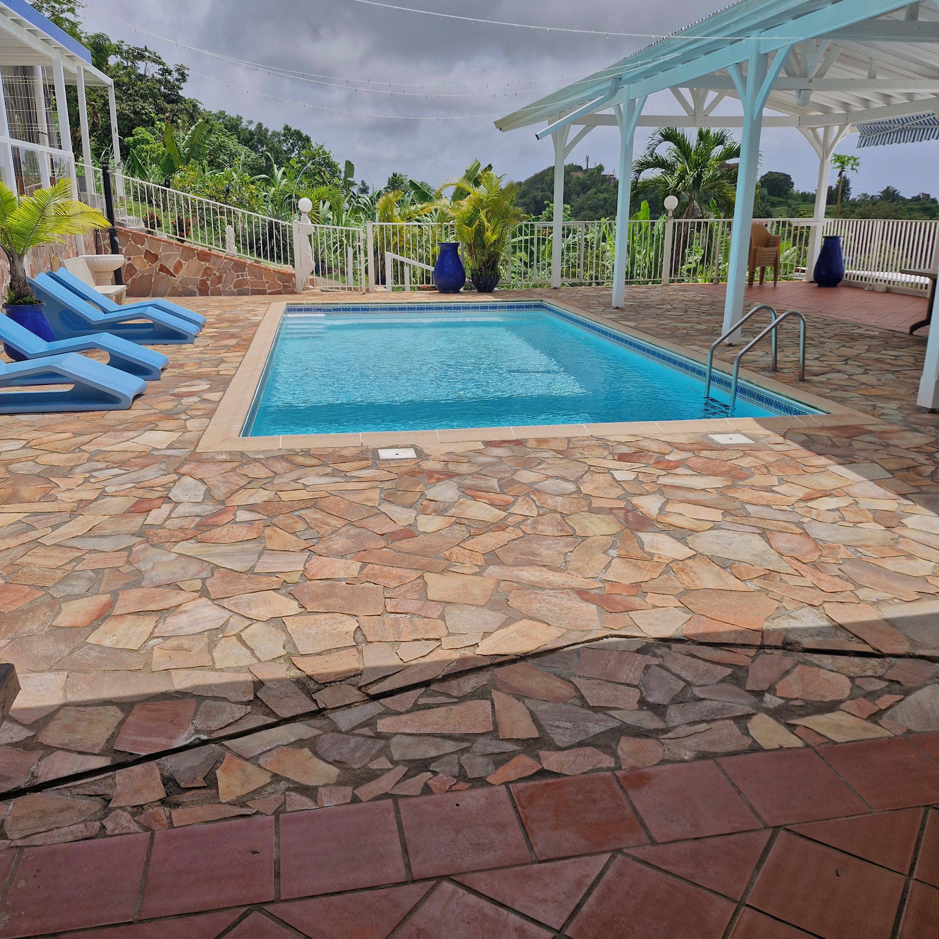A swimming pool with a stone-tiled deck, surrounded by a white fence and potted plants.