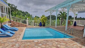 A swimming pool with a stone deck, surrounded by a white fence and potted plants. - VILLA 972 MARINE (Le Vauclin)