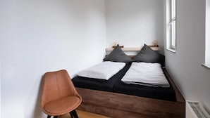 A small, single-bed room with a wooden headboard, a chair, and a window.