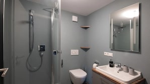 A bathroom with a glass-enclosed shower, a white toilet, a sink with a mirror, and a wooden countertop.