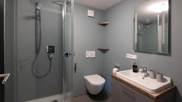 Ein Badezimmer mit einer Duschkabine aus Glas, einer weißen Toilette, einem Waschbecken mit Spiegel und einer Holzauslage.