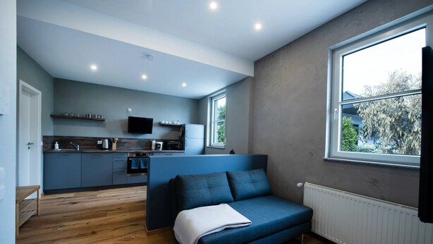 A compact living space with a kitchenette, a sofa, and a large window providing a view of the outdoors.