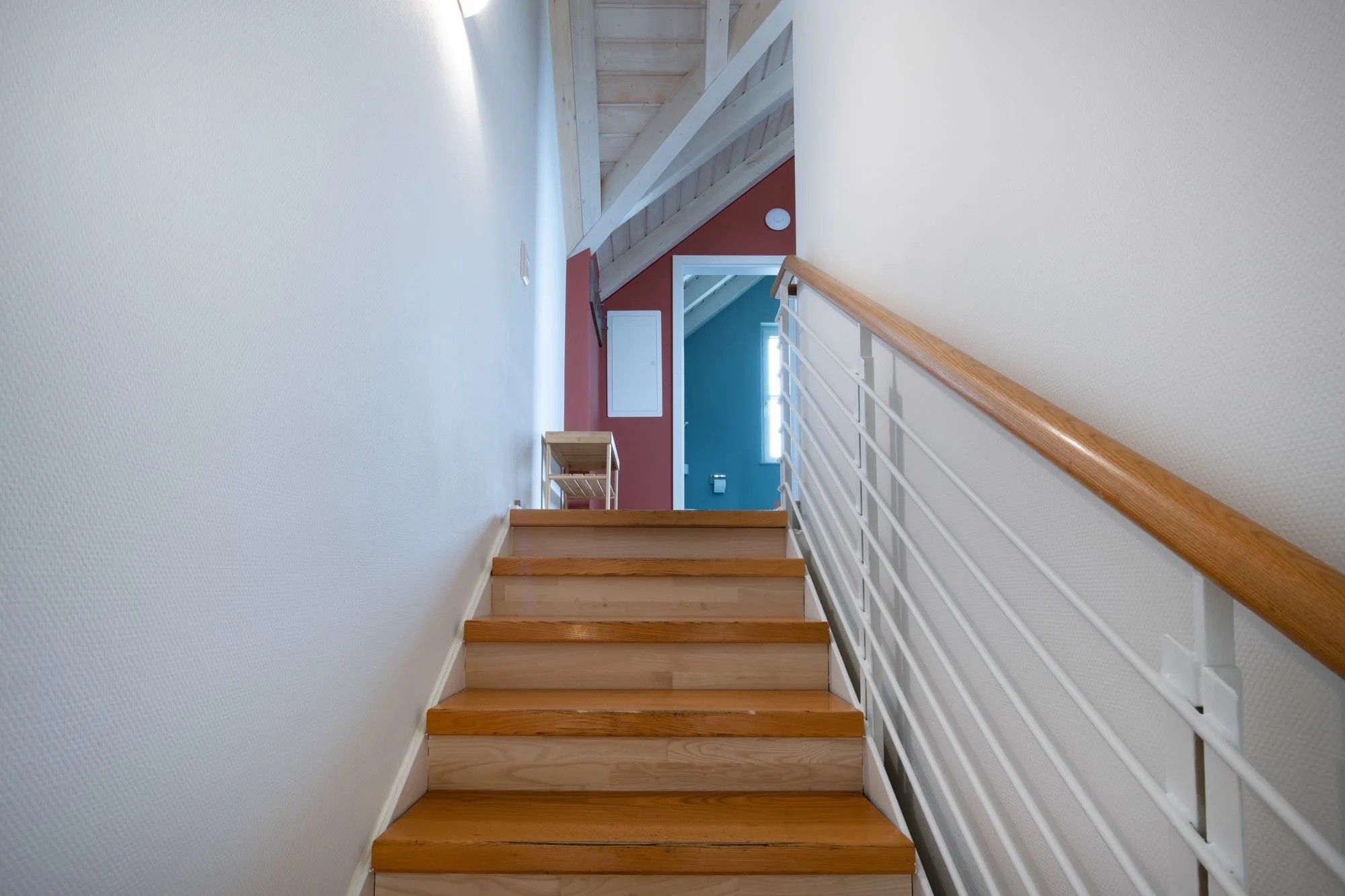 Eine Holztreppe mit weißen Geländern führt zu einem Raum mit einer roten Wand und einer Tür.