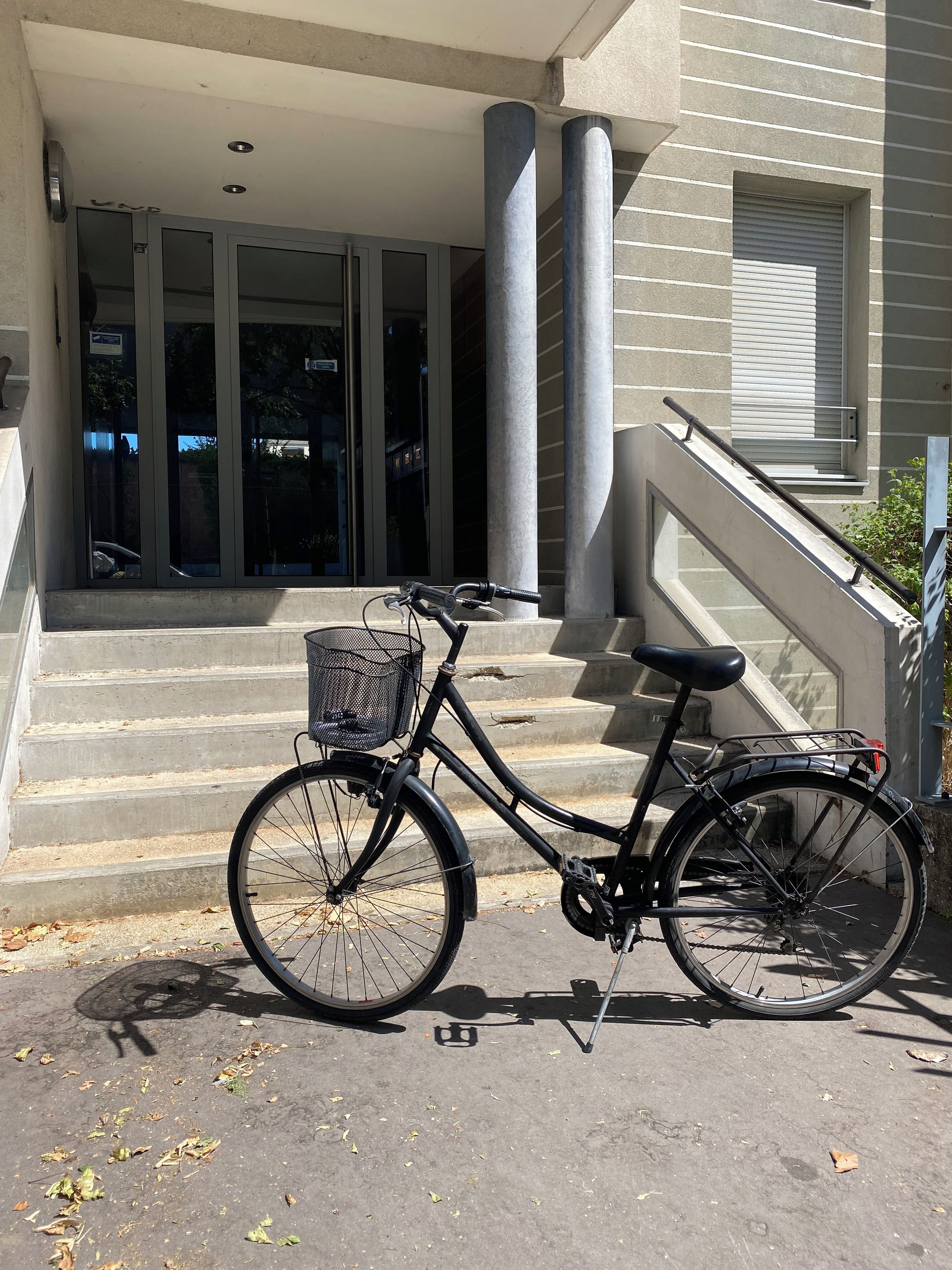 A bicycle parked on concrete steps in front of a building with large columns and a window with blinds.