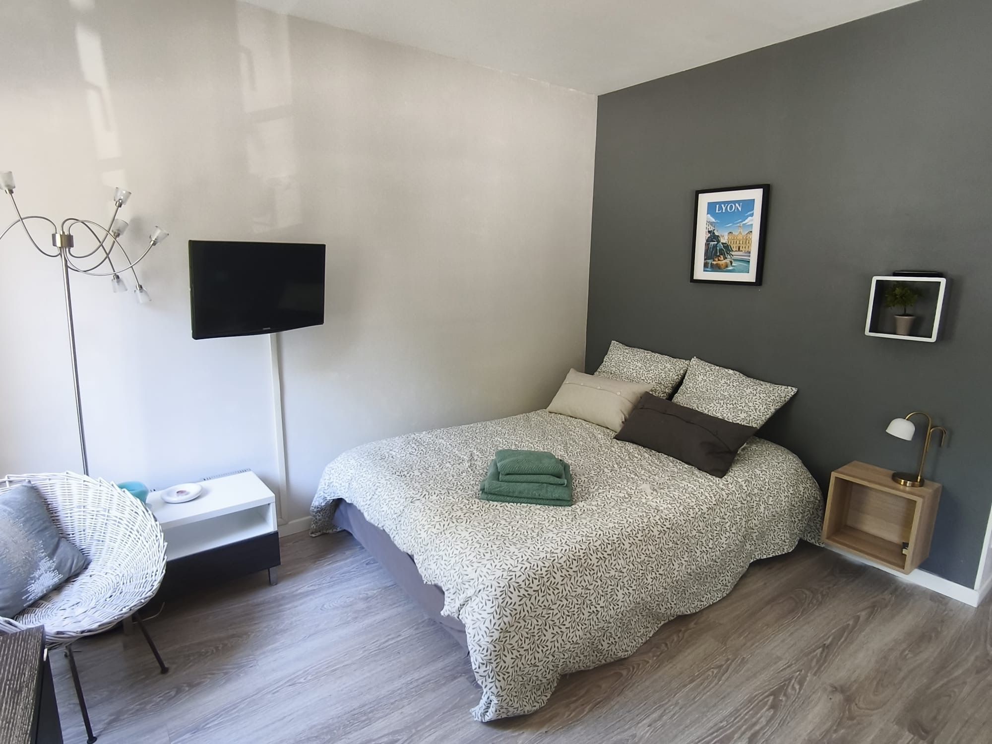A modern bedroom with a bed, a TV, a chair, a bedside table, and a wall-mounted picture.