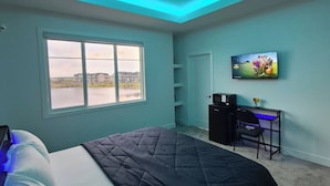 A bedroom with a bed, a desk, a television, and a window with a view of buildings and a body of water. - SwitHome Properties 4BR l 3 baths Lux Escape Near YEG lPond Viewl Game l Triple car Garage. (Leduc)
