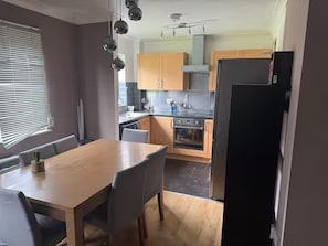 A modern kitchen with wooden cabinets, a dining table, and a black refrigerator. - Apartment Sleeps 4 With Parking (London)