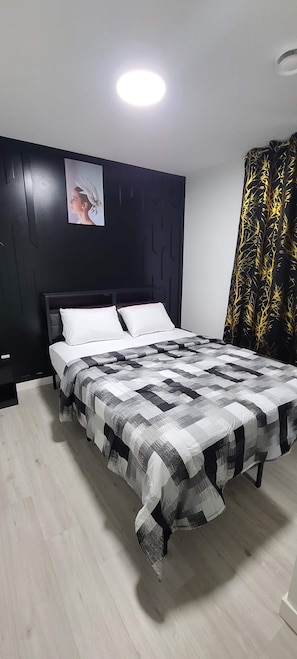 Ein modernes Schlafzimmer mit einem Bett, einem Kopfteil, einem Wandbild und einem gemusterten Vorhang.