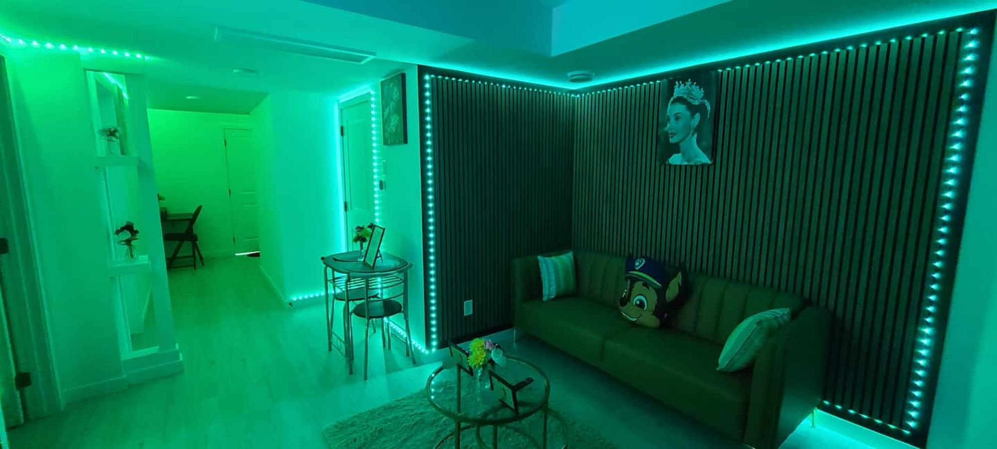 A room with a green-lit wall, a sofa, a coffee table, and a small table with a picture frame.