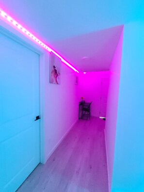 A narrow hallway with a white door on the left, a small table with a chair in the center, and a door at the end. - SwitHome Properties Glen Cozy Suite Near Yeg Airport (Edmonton)