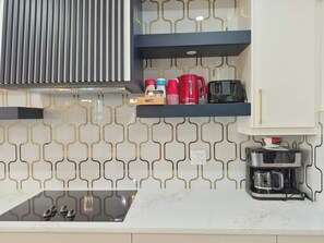 A modern kitchen with a built-in stove, a coffee maker, and a shelf with red and white cups. - SwitHome Properties Luxury 3BR l 3baths Near YEGl Pondview l Games l With Triple Car  Garage (Leduc)