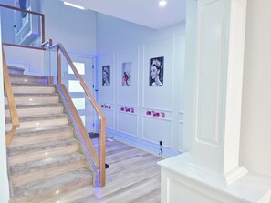 A staircase with wooden handrails and a light wood floor, leading to a landing with a white wall and framed pictures. - SwitHome Properties Luxury 3BR l 3baths Near YEGl Pondview l Games l With Triple Car  Garage (Leduc)