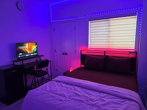 A bedroom with a bed, a desk with a computer, a chair, a window with blinds, and LED strip lighting. - SwitHome Properties Luxury 3BR l 3baths Near YEGl Pondview l Games l With Triple Car  Garage (Leduc)