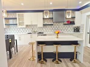 A modern kitchen with white cabinets, a central island with stools, and a patterned backsplash. - SwitHome Properties Luxury 3BR l 3baths Near YEGl Pondview l Games l With Triple Car  Garage (Leduc)