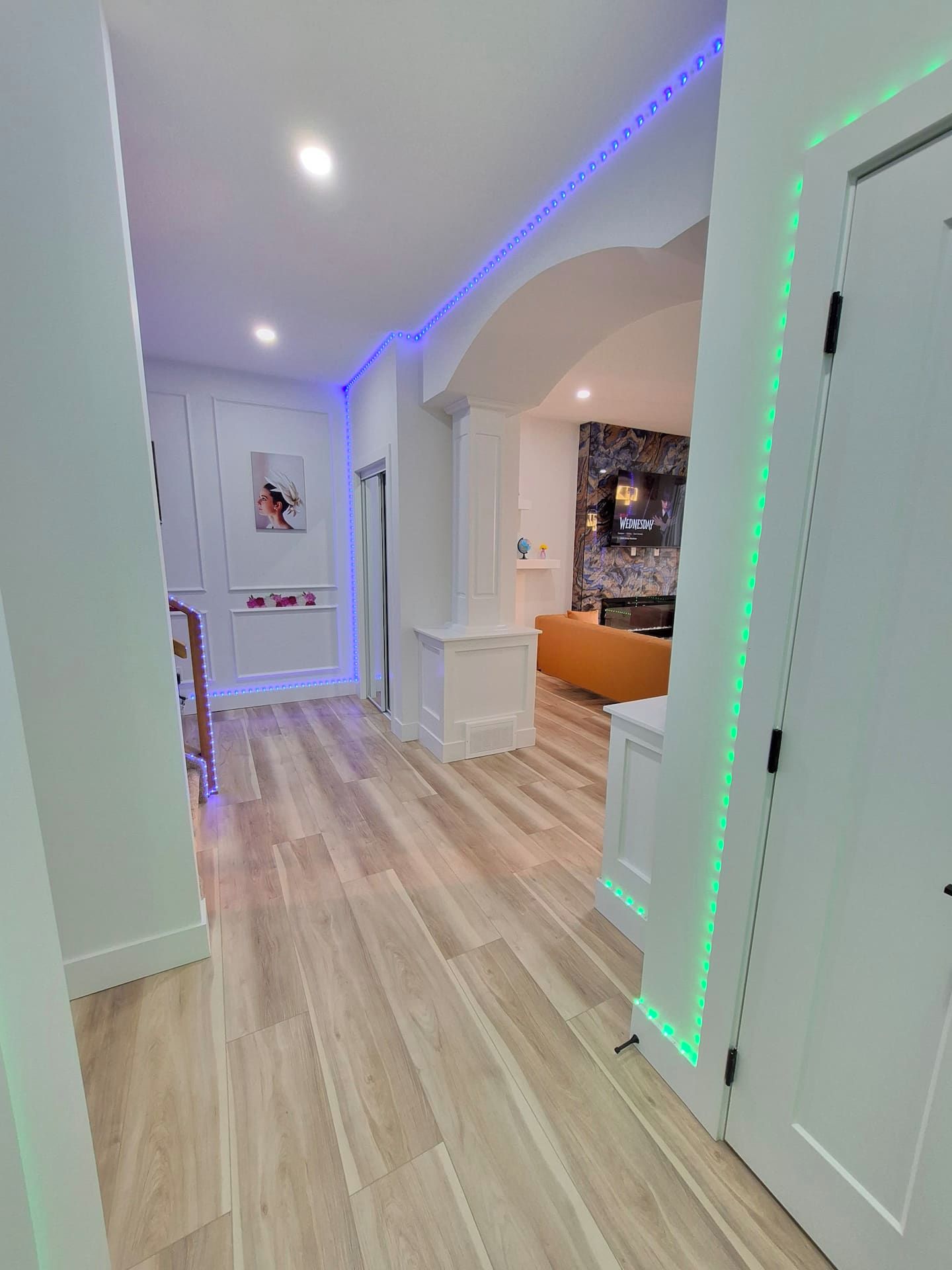 Um corredor com piso de madeira, paredes brancas e uma porta iluminada com luzes LED verdes.