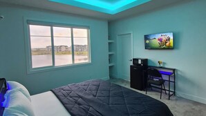 Una camera da letto con un letto, una scrivania, una televisione e una finestra vista edifici e un corpo d'acqua.
