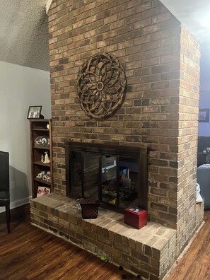 A brick fireplace with a decorative metal piece above it, a shelf with various items, and a red box on the mantel.