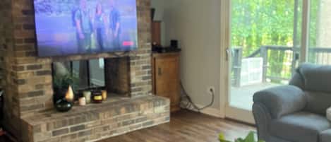 Un salon avec un téléviseur à écran plat fixé à un mur en briques, une table basse en verre et un canapé gris.