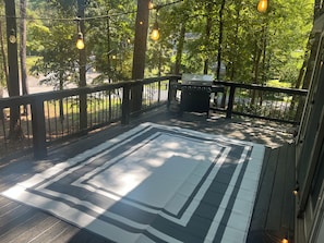 Eine Terrasse mit einem schwarz-weiß gestreiften Teppich, einem Grill und hängenden Lampen.