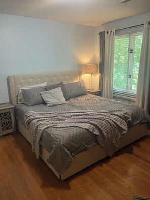 Ein Schlafzimmer mit einem großen Bett, einem Nachttisch, einer Lampe und einem Fenster mit Vorhängen.