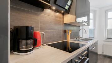 Une cuisine moderne avec une machine à café noire, une bouilloire rouge et une cuisinière encastrée.