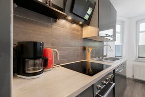 Una cocina moderna con una cafetera negra, un hervidor rojo y una estufa empotrada.