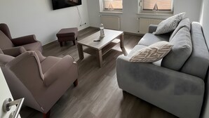 Uma sala de estar moderna com sofá, poltrona, mesa de centro e TV de tela plana fixada na parede.