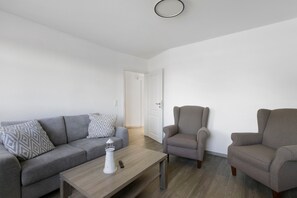 En moderne stue med en grå sofa, to lænestole, et sofabord og en hvid dør i baggrunden.