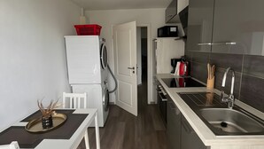 Cozinha compacta com área de refeições, máquina de lavar e micro-ondas.