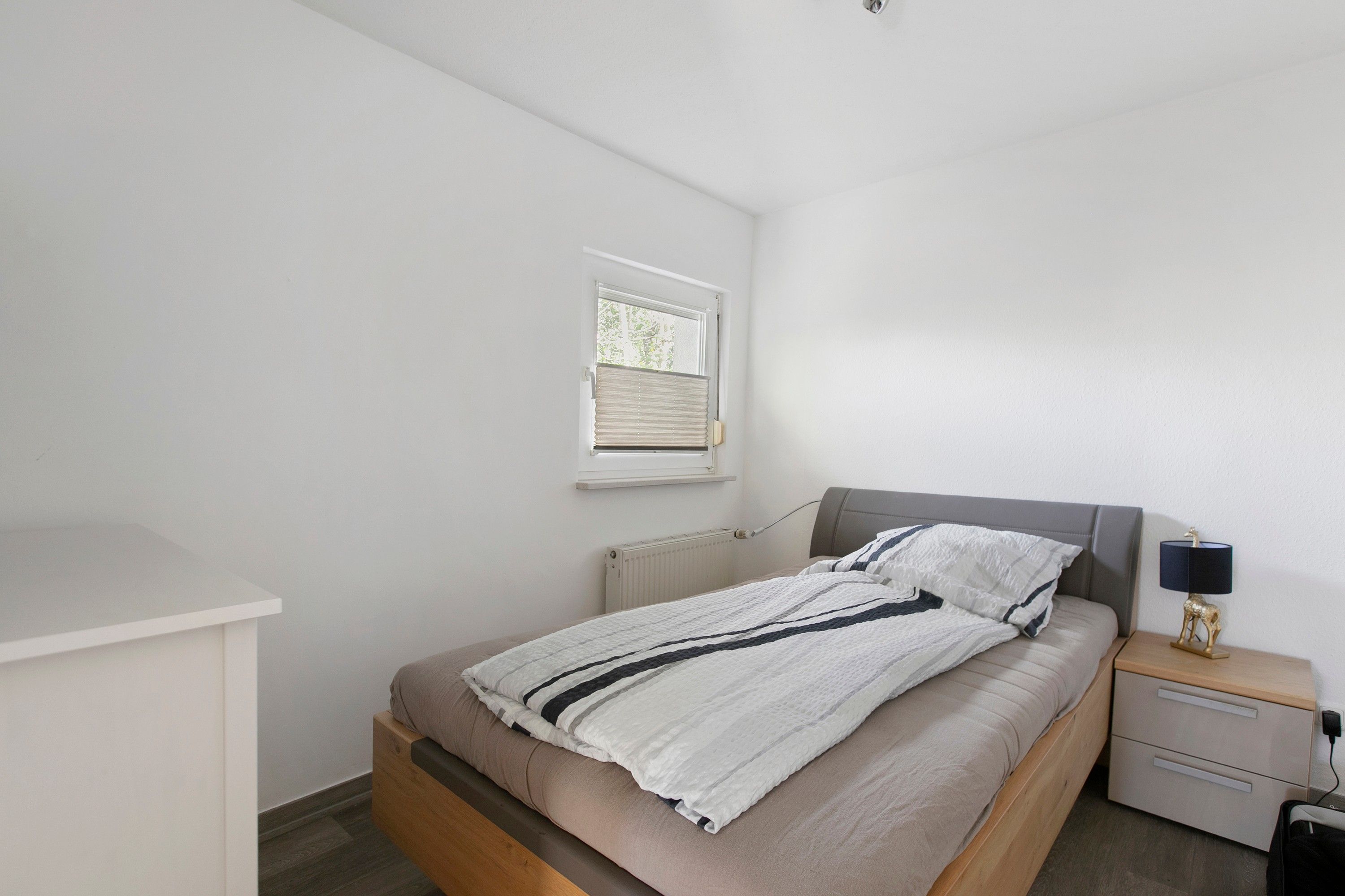 Une chambre à coucher avec un lit, une table de chevet, une lampe et une fenêtre.