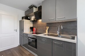 Une cuisine moderne avec des meubles gris, un évier en acier inoxydable et un four encastré.