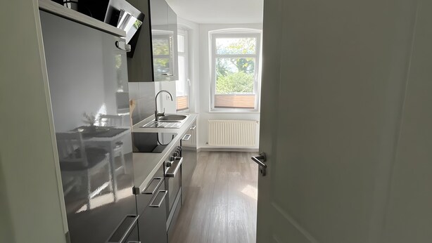 Cozinha moderna com eletrodomésticos de aço inoxidável, janela com vista para área verde e porta que dá para outro cômodo.