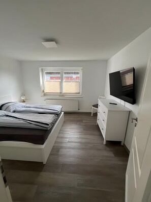 Et soveværelse med seng, skrivebord, fjernsyn og et vindue med skodder.
