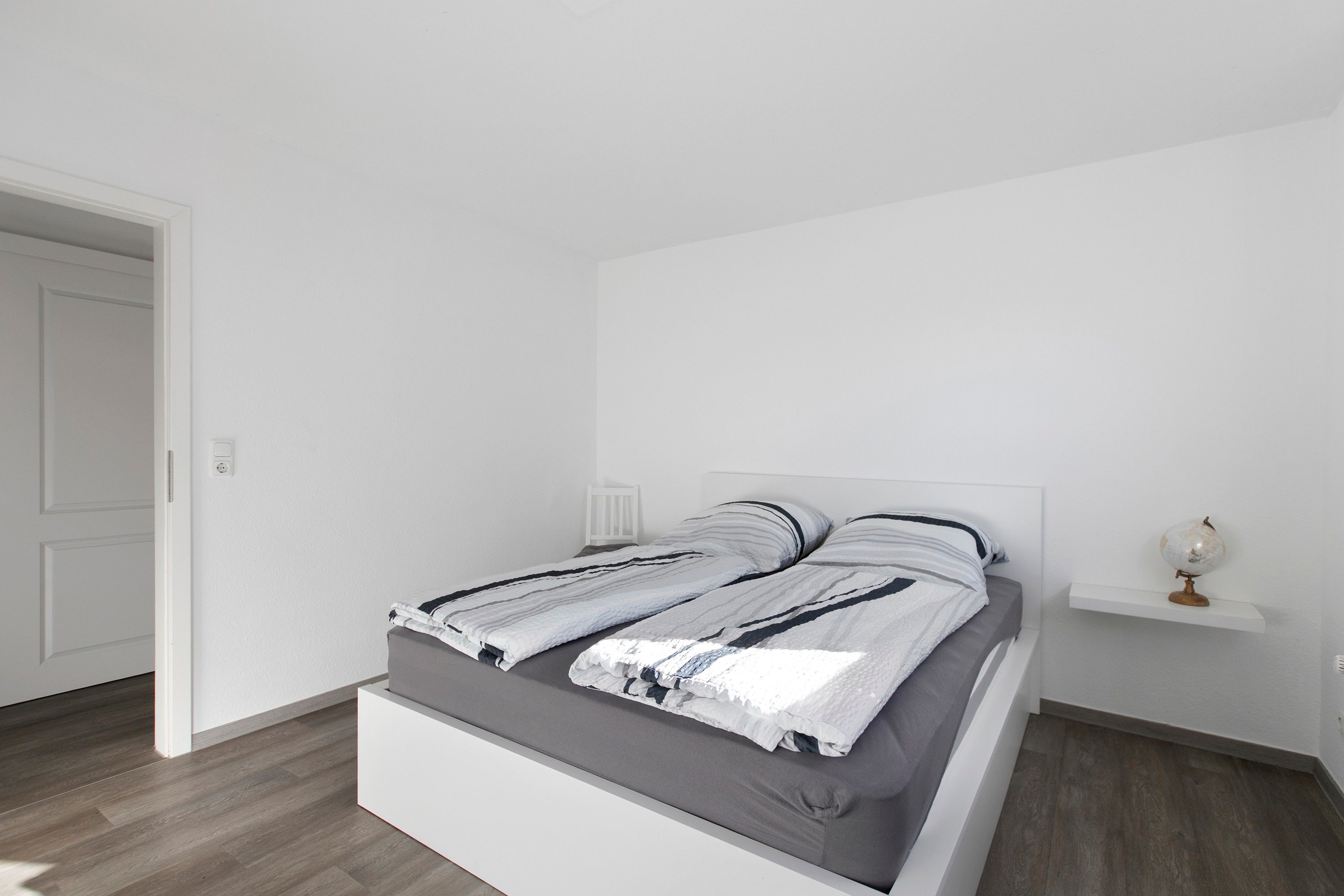 Ein modernes Schlafzimmer mit einem Bett, einem Nachttisch und einem Globus auf einem Regal.