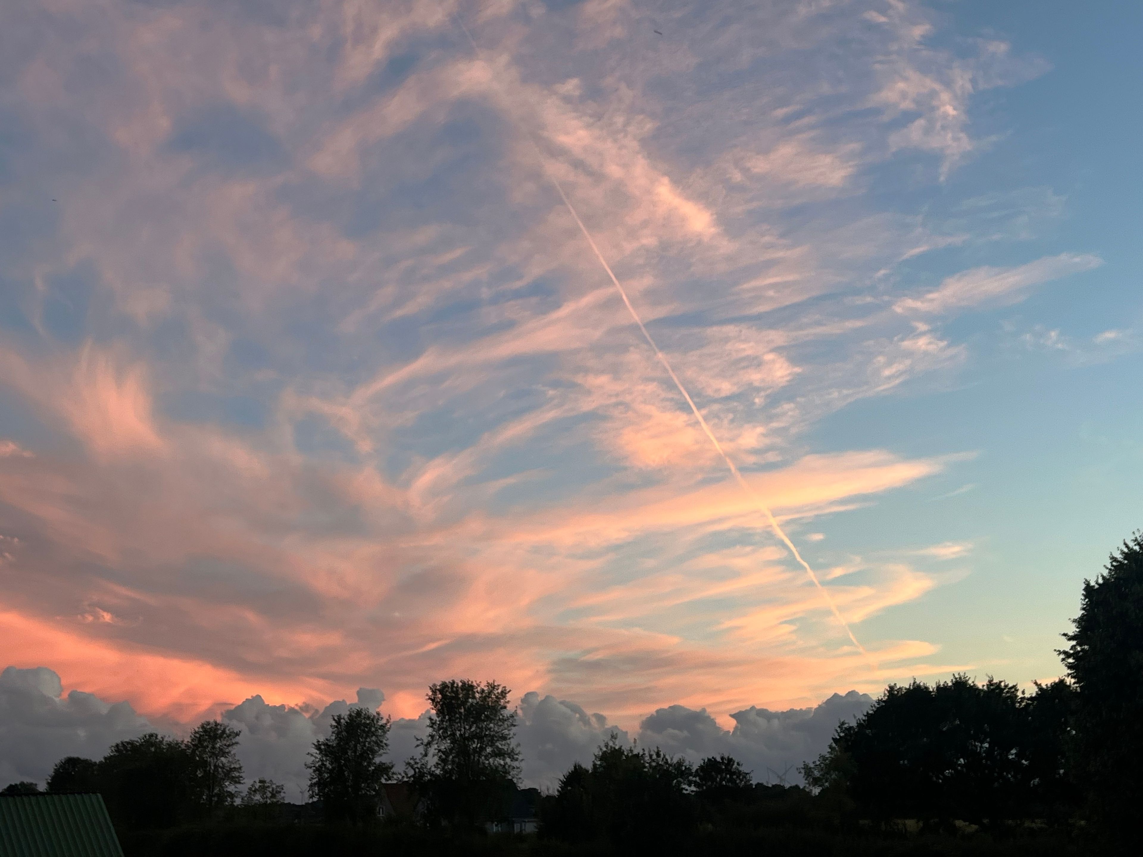 Un ciel au coucher du soleil, avec des nuages et une traînée de condensation.