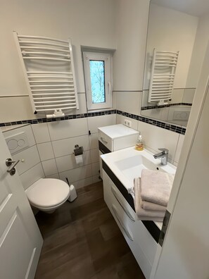 Et lille badeværelse med toilet, håndvask og spejl.