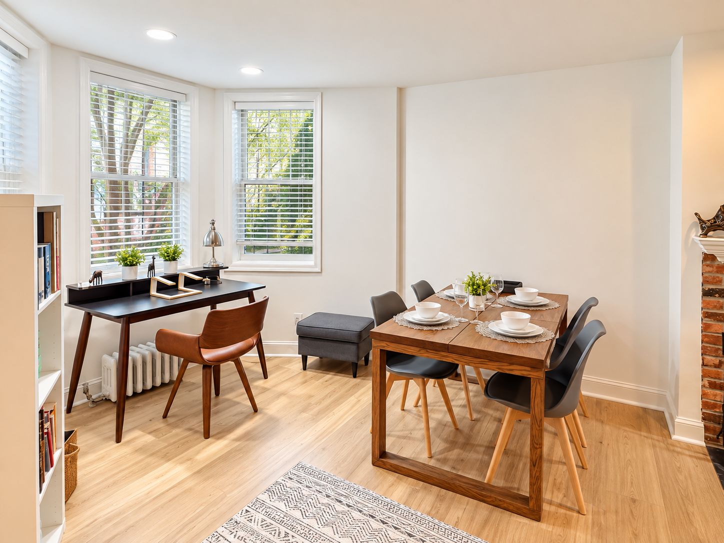 A dining area with a wooden table set for four, surrounded by chairs, in a room with hardwood flooring and white walls.