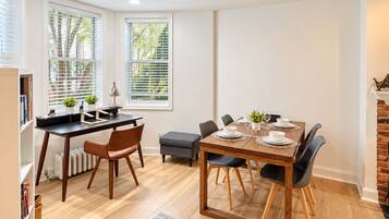 A dining area with a wooden table set for four, surrounded by chairs, in a room with hardwood flooring and white walls.