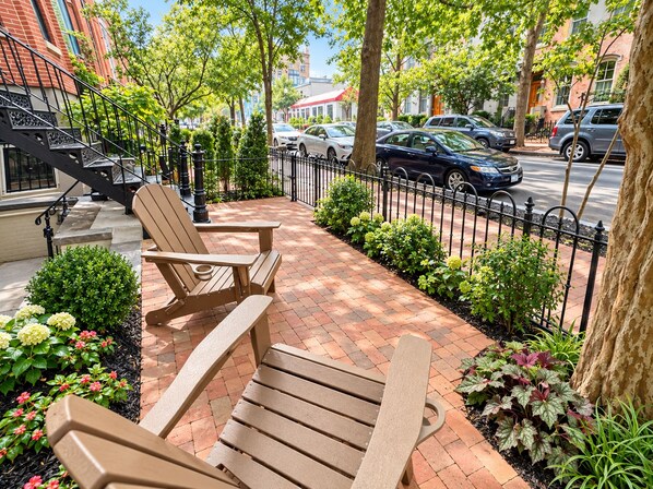 A brick-paved outdoor seating area with Adirondack chairs, a metal fence, and a row of parked cars. - 1BR in Logan Circle - DC Metro - We Host (Washington)