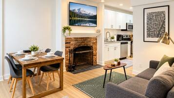 A modern living space with a dining area, fireplace, kitchen, and a grey sofa.