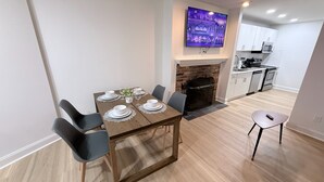 A dining area with a wooden table set for four, a fireplace, and a kitchen in the background. - 1BR in Logan Circle - DC Metro - We Host (Washington)