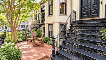 A residential building with a brick pathway, a wooden bench, and a staircase with ornate metal railings.