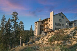 Un immeuble à plusieurs étages doté d’un balcon, entouré d’arbres et de rochers.