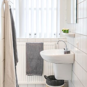 A bathroom with a white sink, a towel rack with two towels, a radiator, and a small shelf with a plant. - Landgoed 't Borghuis - De Boomgaard | 4–16 people (Losser)