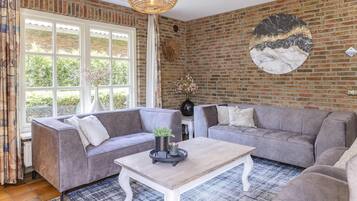 Een woonkamer met een bakstenen muur, twee grijze banken, een witte salontafel en een hangende lamp.