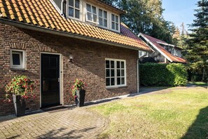 A brick house with a tiled roof, a front door, and two windows. There are potted plants in front of the house.