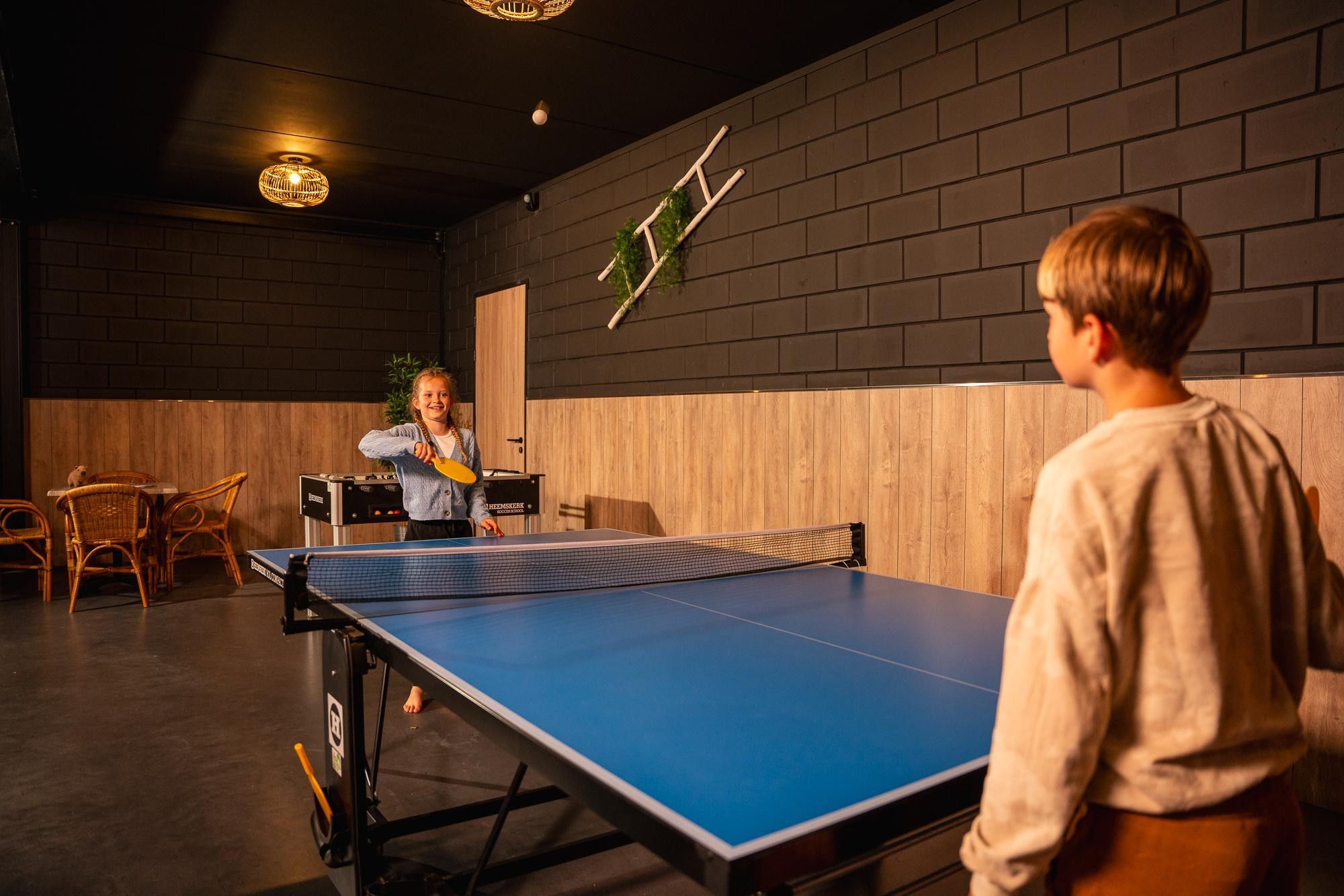 Una mesa de ping pong con red en una habitación con paredes de ladrillo y paneles de madera.