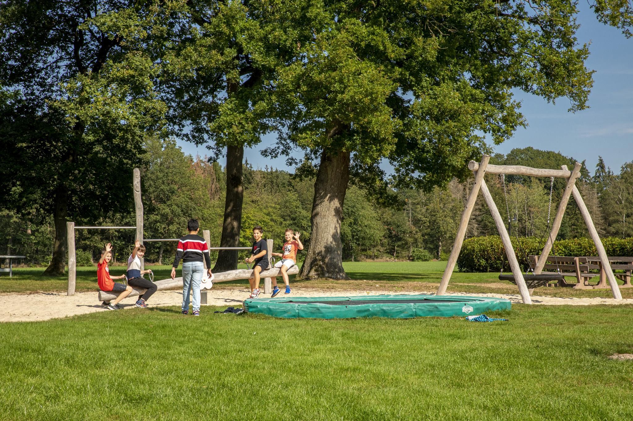 A playground with a swing set, a trampoline, and a sandpit.