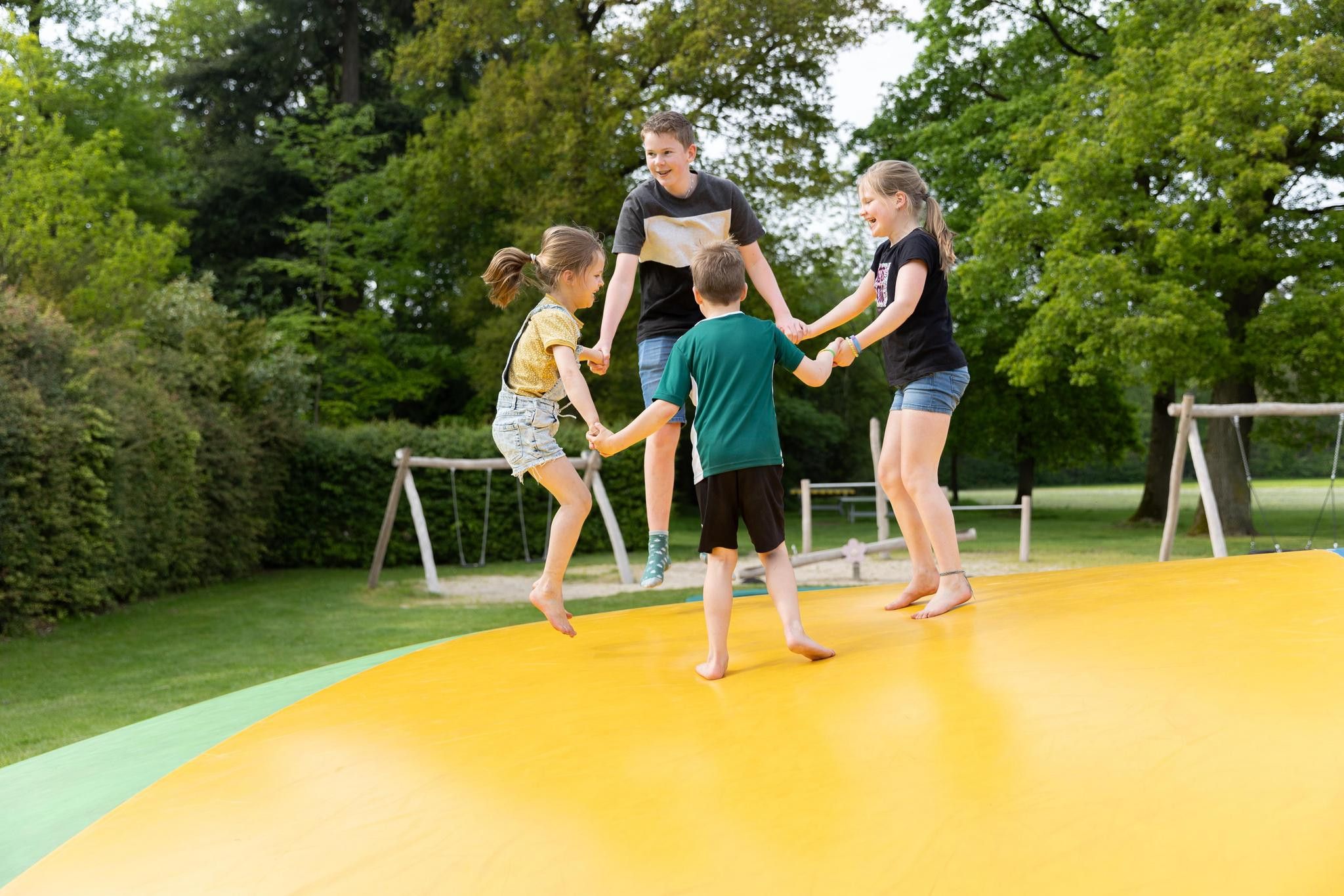A group of people on a yellow outdoor play area with trees in the background.